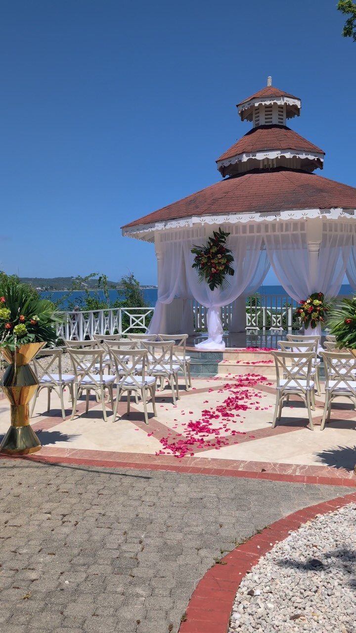 White wedding gazebo with brown roof overlooking the ocean with petal-strewn patio.