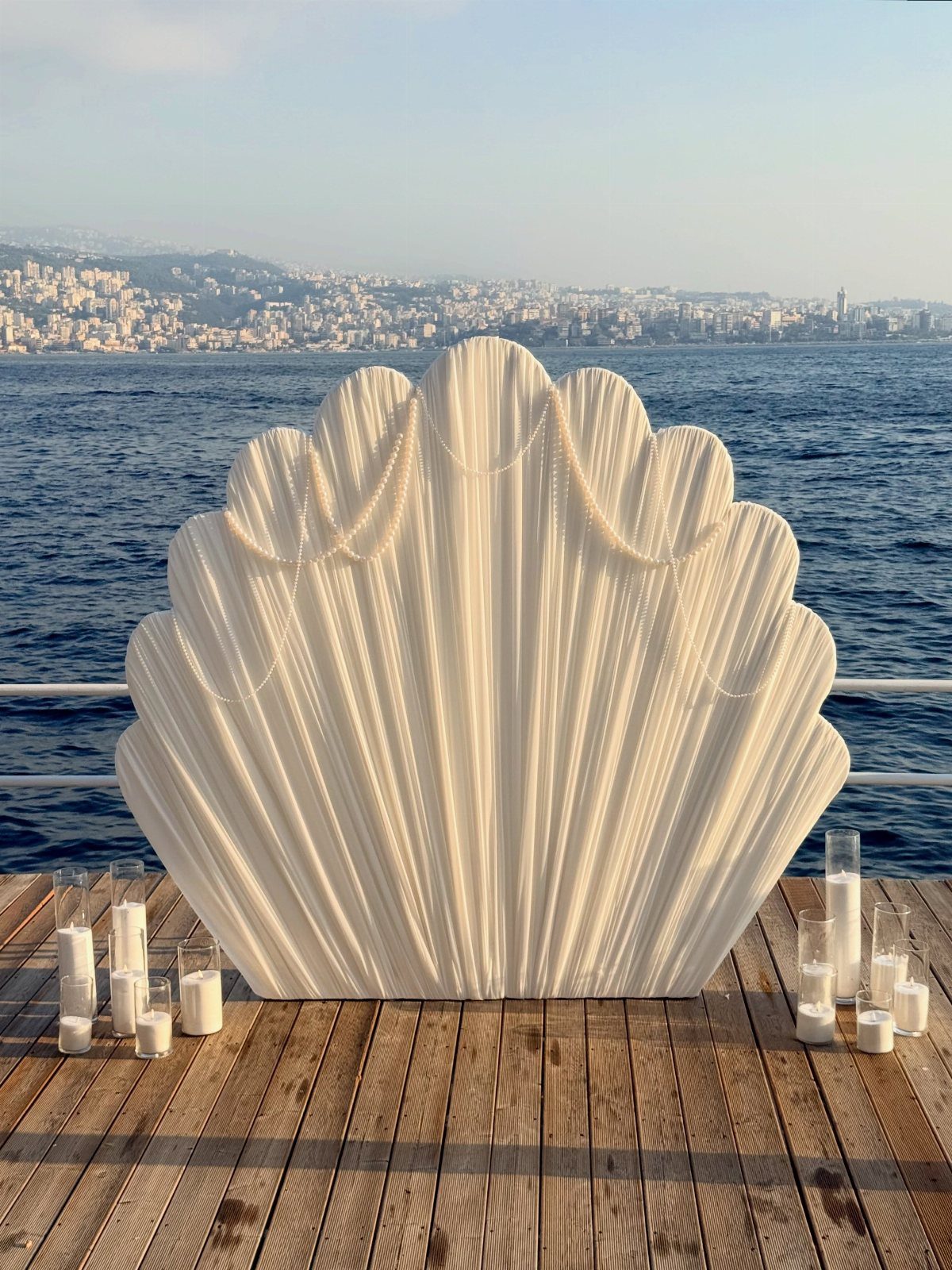 White shell-shaped backdrop with candles on a wooden deck by the ocean