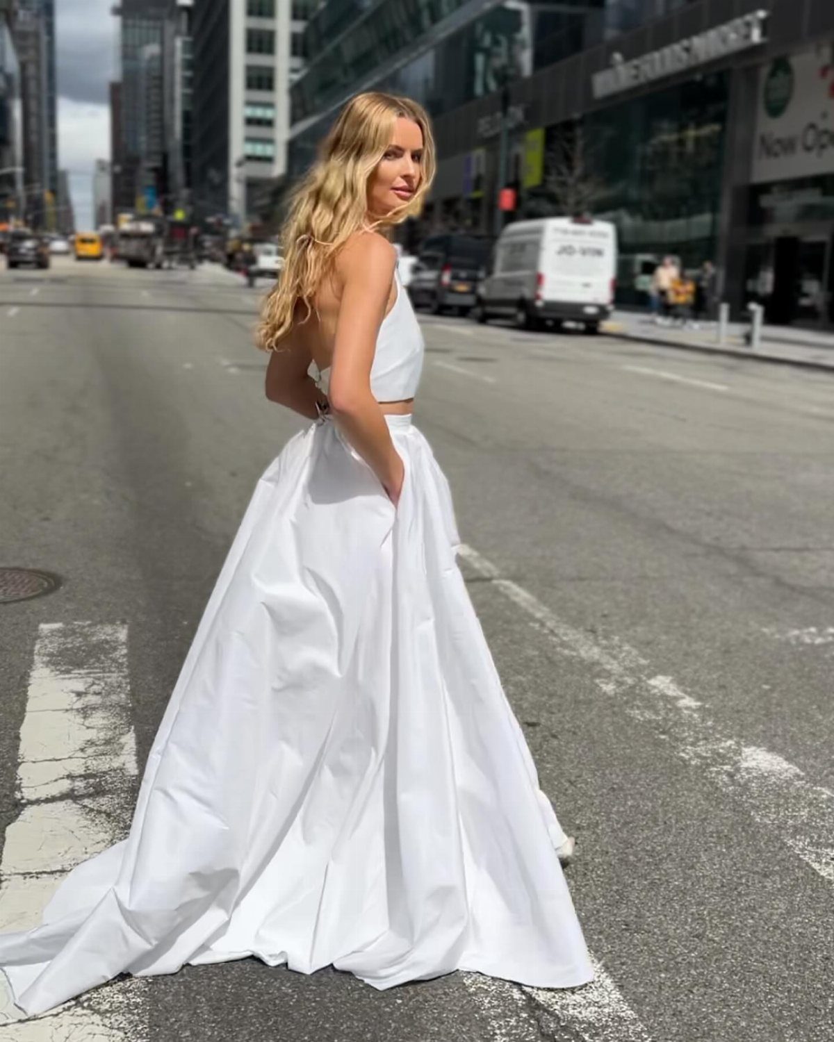 Woman wearing a white cropped top and full white skirt on city street