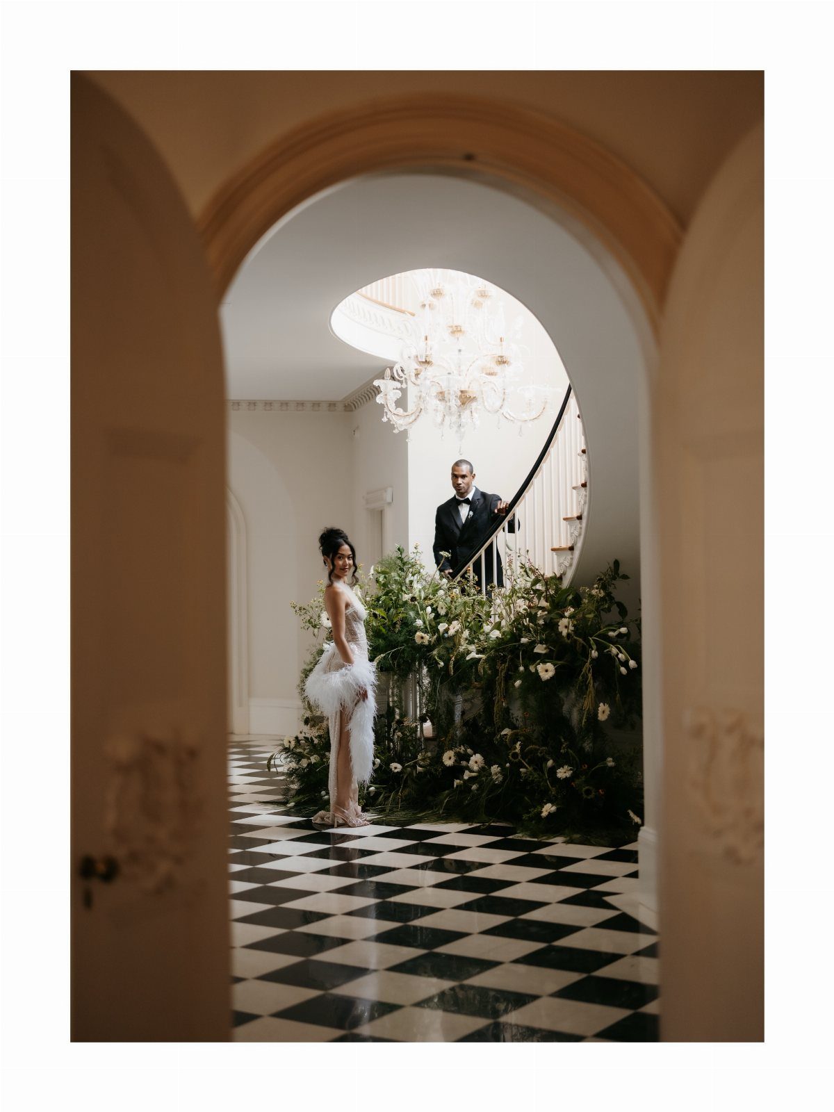 Woman in white feathered cocktail dress and man in tuxedo in grand hall
