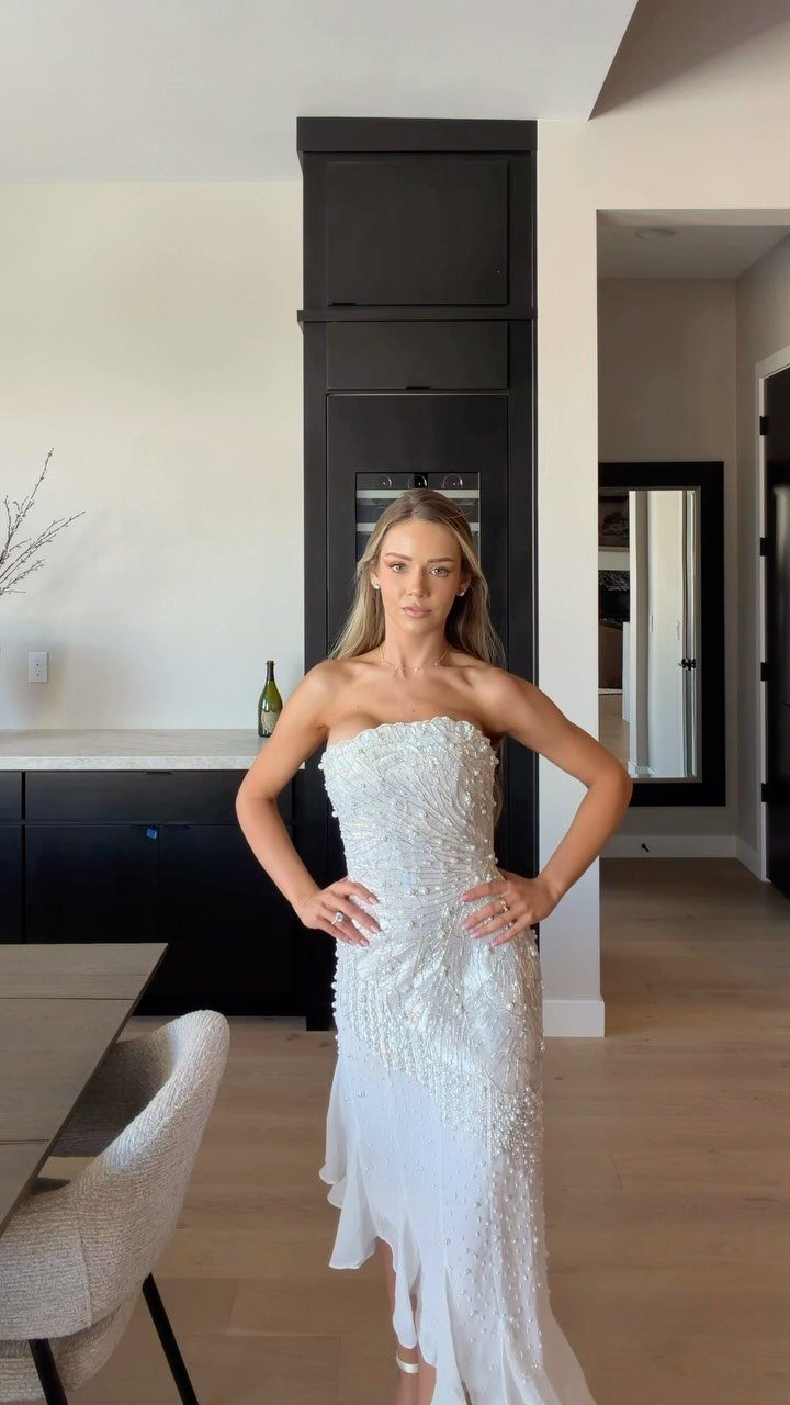 Woman in a white strapless beaded high-low wedding dress posing in a modern room