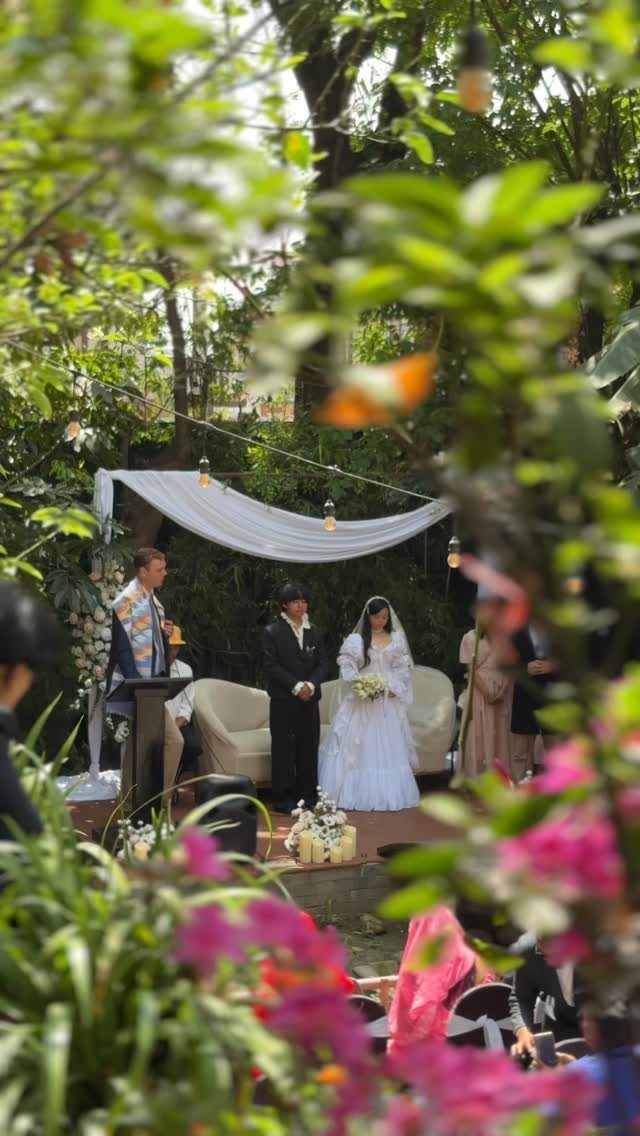 Bride and groom standing under a white canopy in a green garden venue.