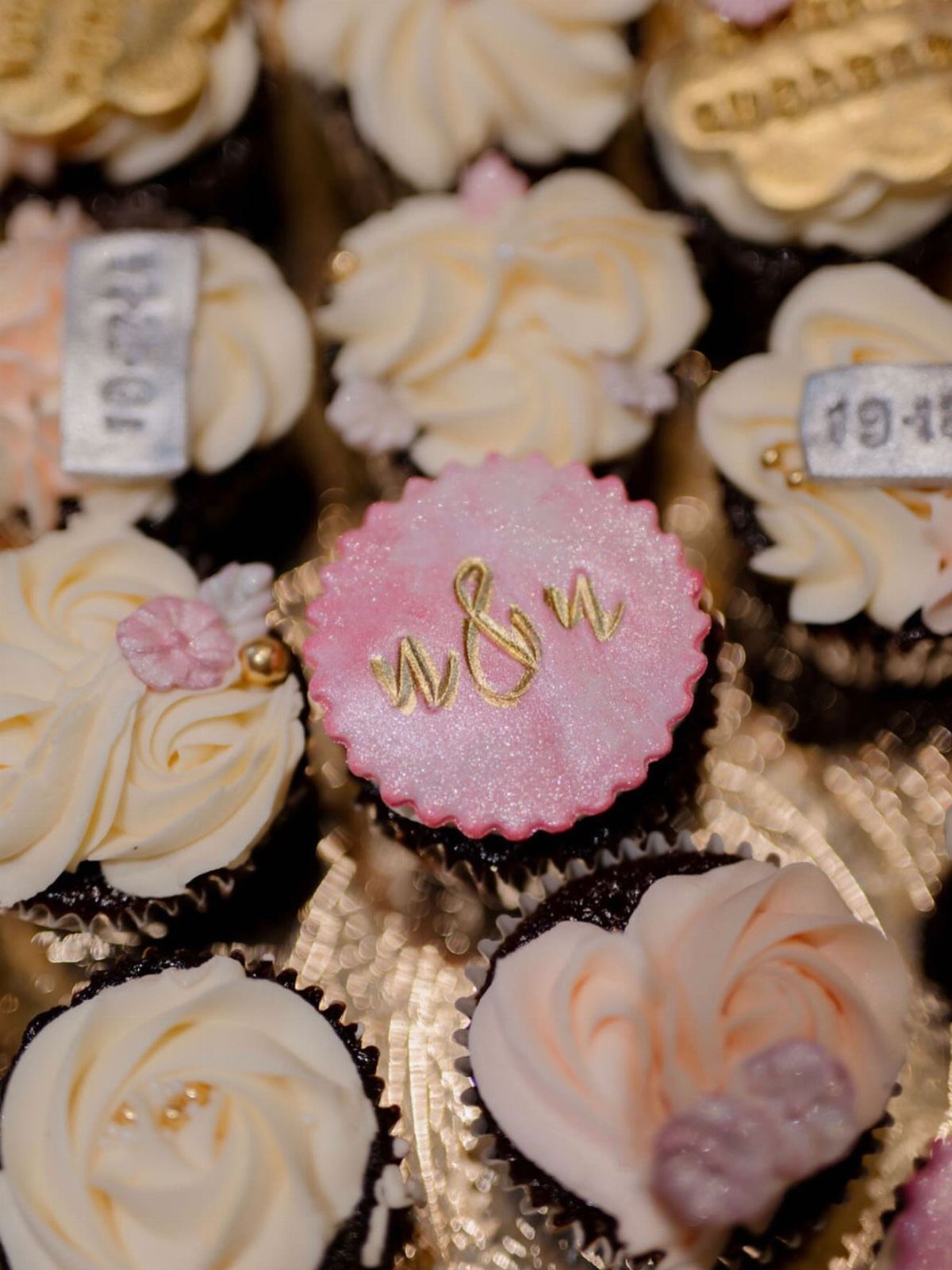 Chocolate cupcakes with pink and white frosting and gold initials on a topper.