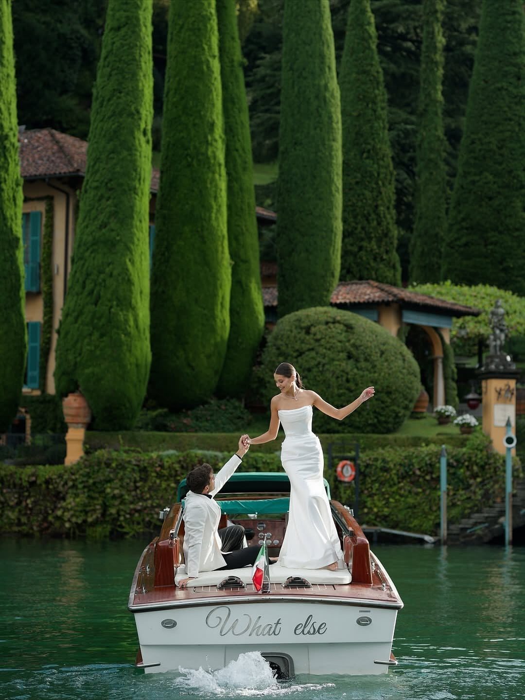 Bride and groom posing on a wooden boat on a lake with cypress trees.