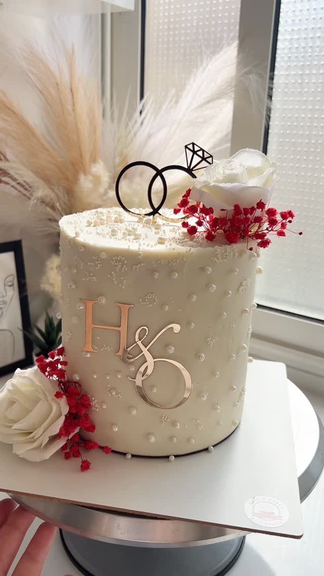 Small white wedding cake with pearls, red flowers, and gold monogram initials.
