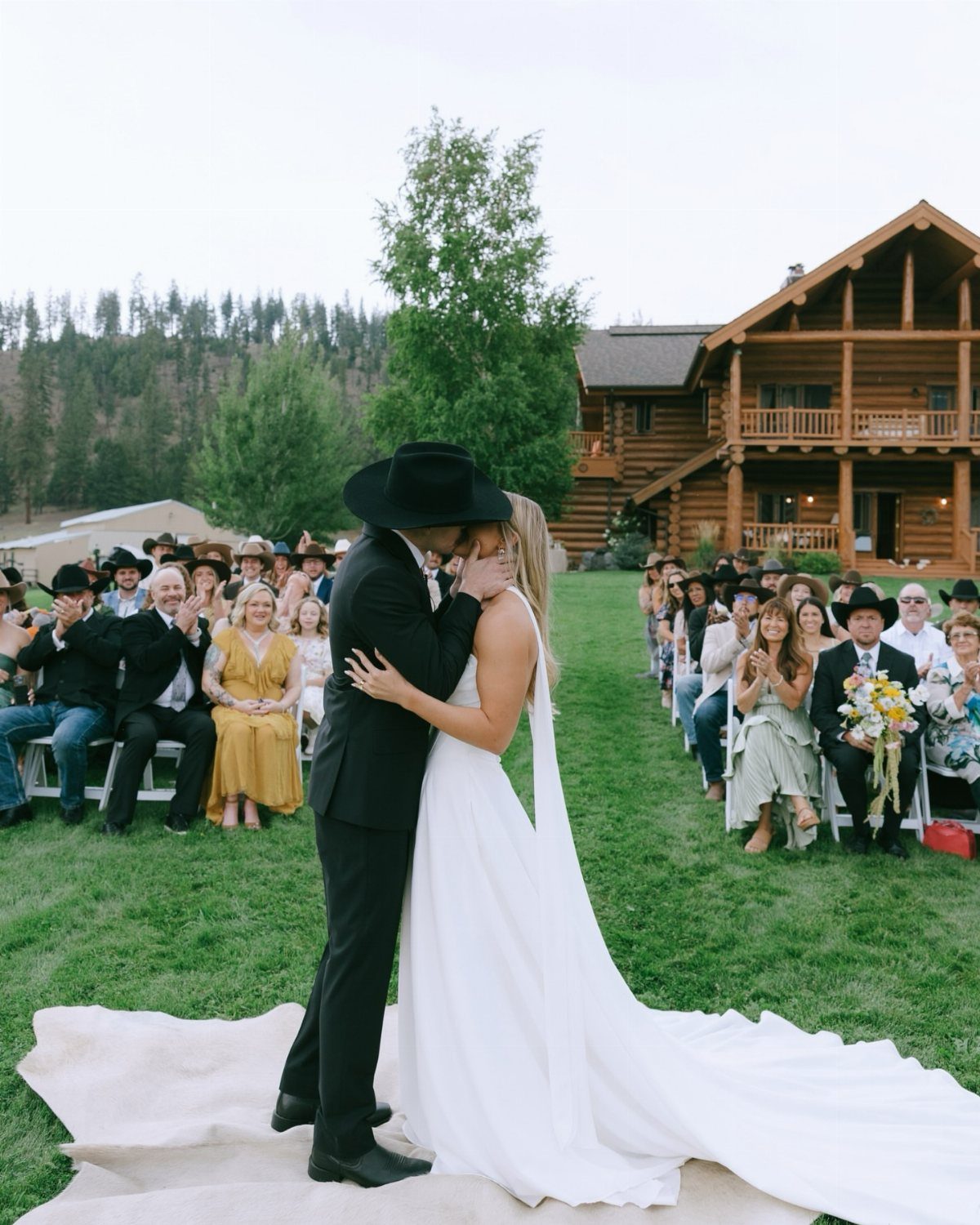 Bride and groom kissing on a rug before guests at a log cabin venue