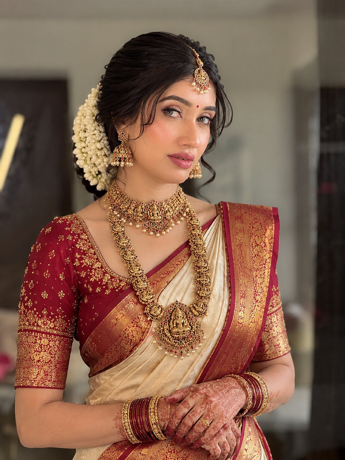 South Indian bride in cream and maroon silk saree with ornate gold jewelry