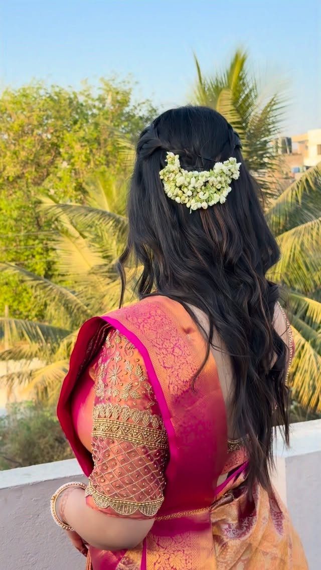 Woman from behind in a pink and gold silk saree with floral hair accessories.