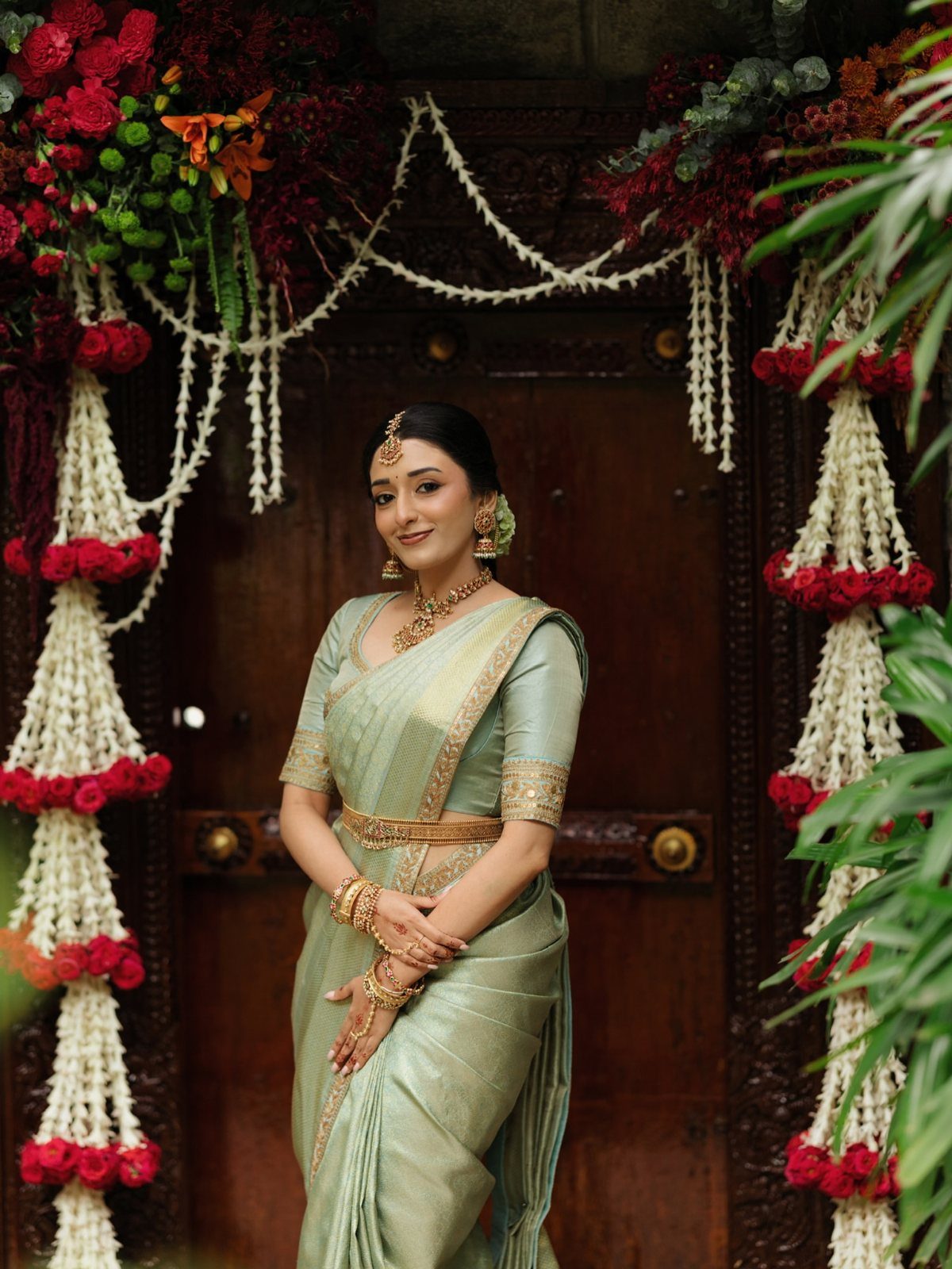 South Indian bride in a light green silk saree and gold jewelry posing outdoors