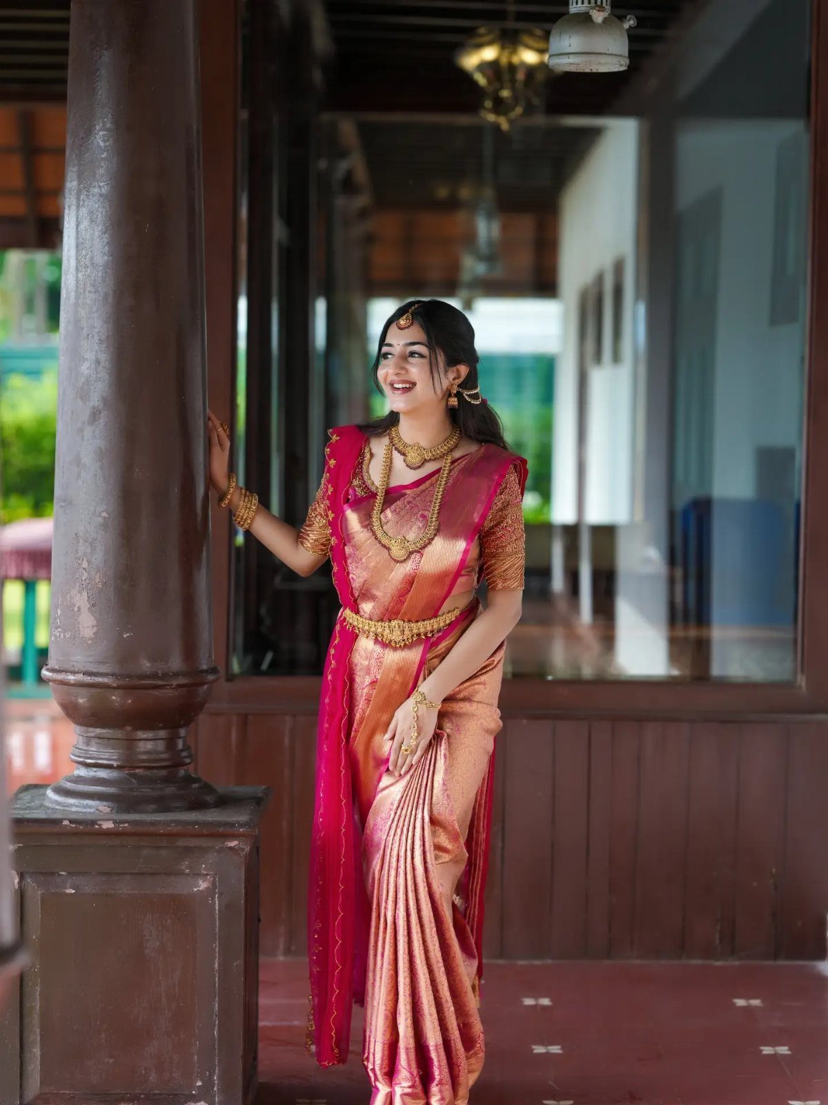 Woman in red and gold silk saree with traditional gold temple jewelry posing outdoors.