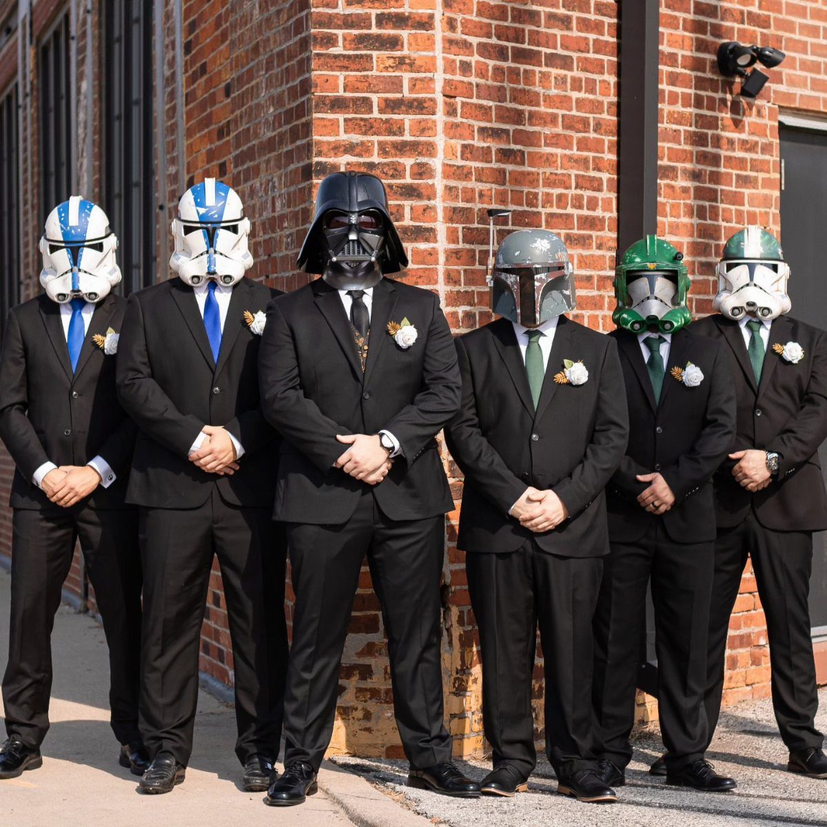 Men in black suits wearing Star Wars helmets posing against a brick wall.