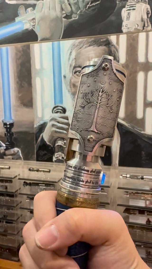 Silver metal lightsaber hilt with tree engraving held by a hand