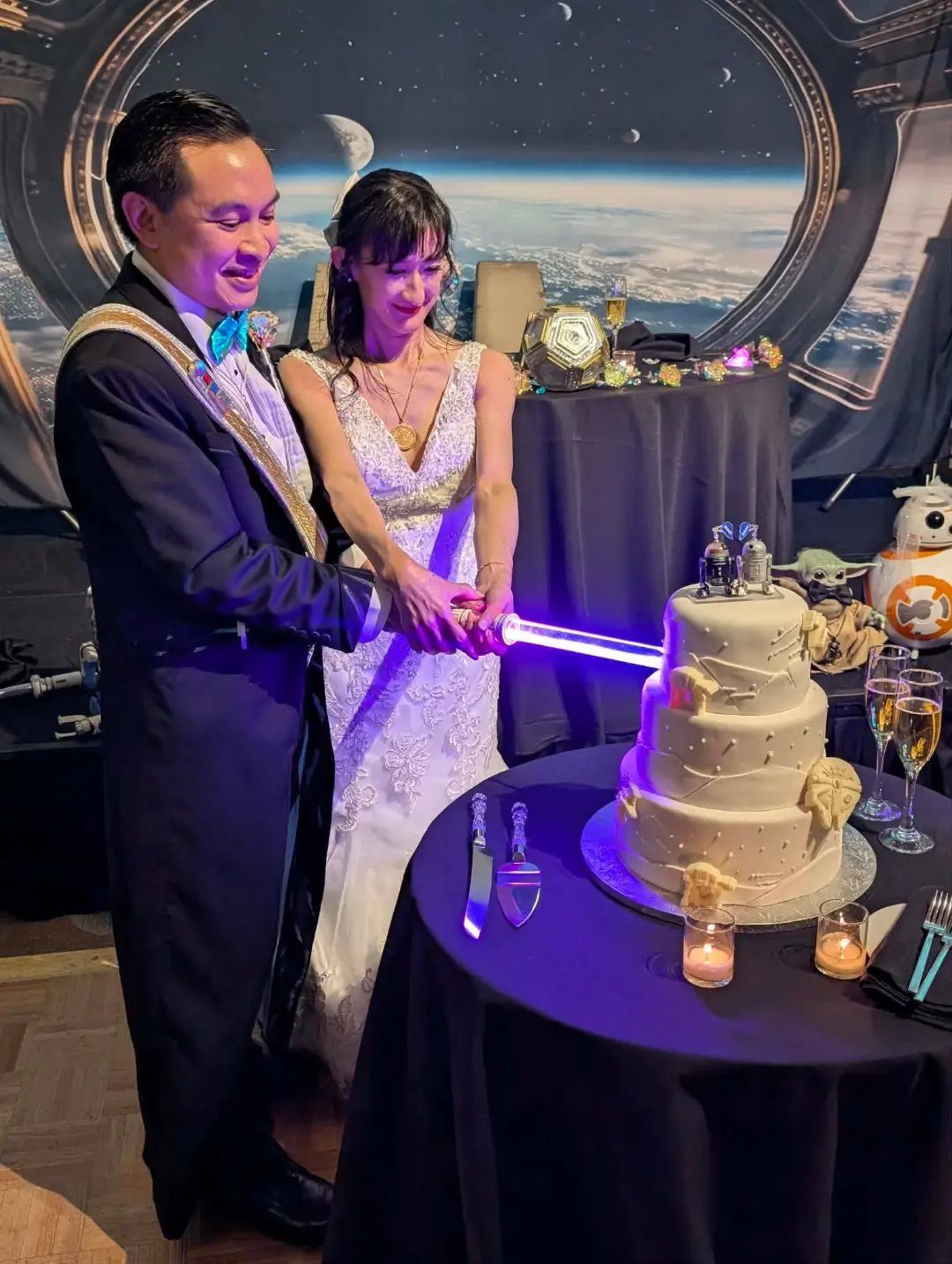 Bride and groom cutting a wedding cake with a blue glowing lightsaber
