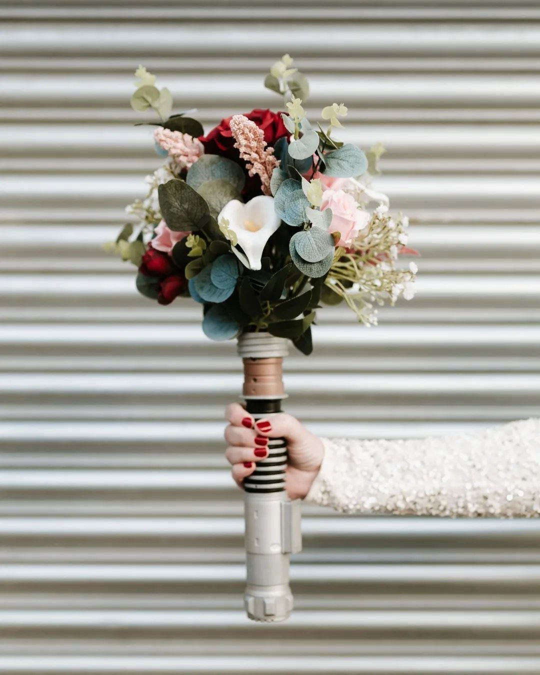 Floral bouquet with red and white flowers held by a lightsaber hilt handle.