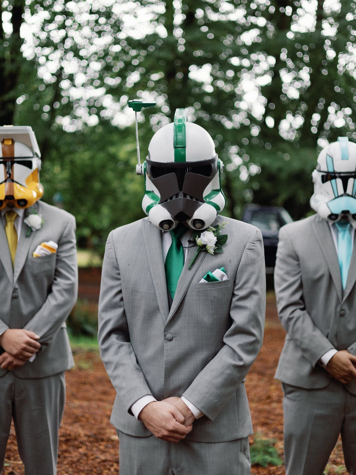 Three men in grey suits wearing Star Wars clone trooper helmets in a forest