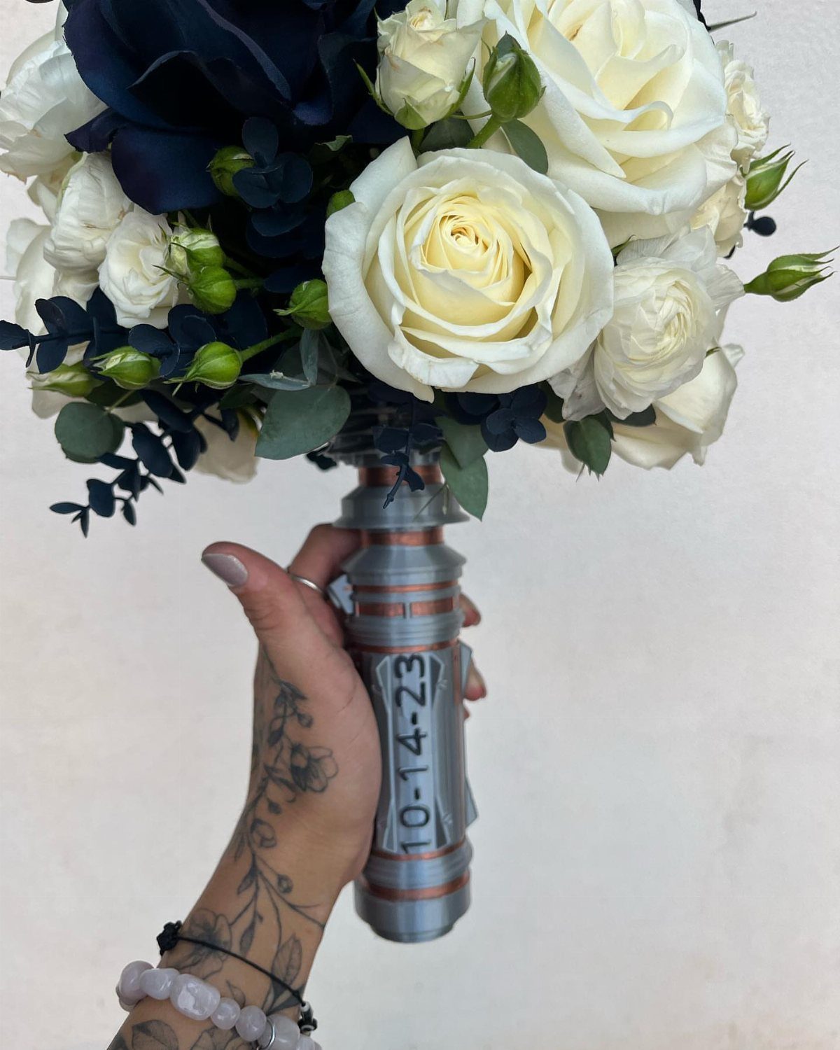 Bridal bouquet of white and blue roses with a lightsaber hilt handle.