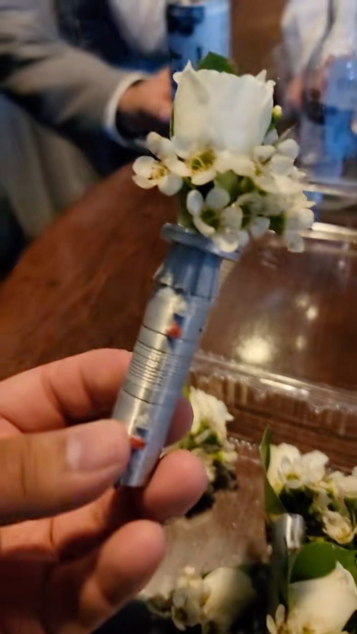 Lightsaber hilt boutonniere with white roses and baby's breath held by a hand.