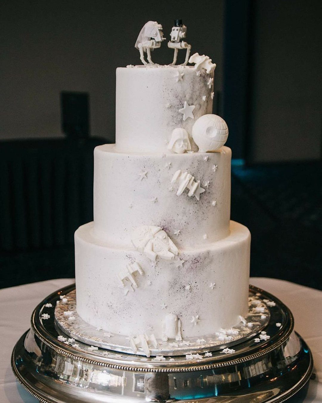 Three-tiered white wedding cake decorated with Star Wars characters and ships on silver platter