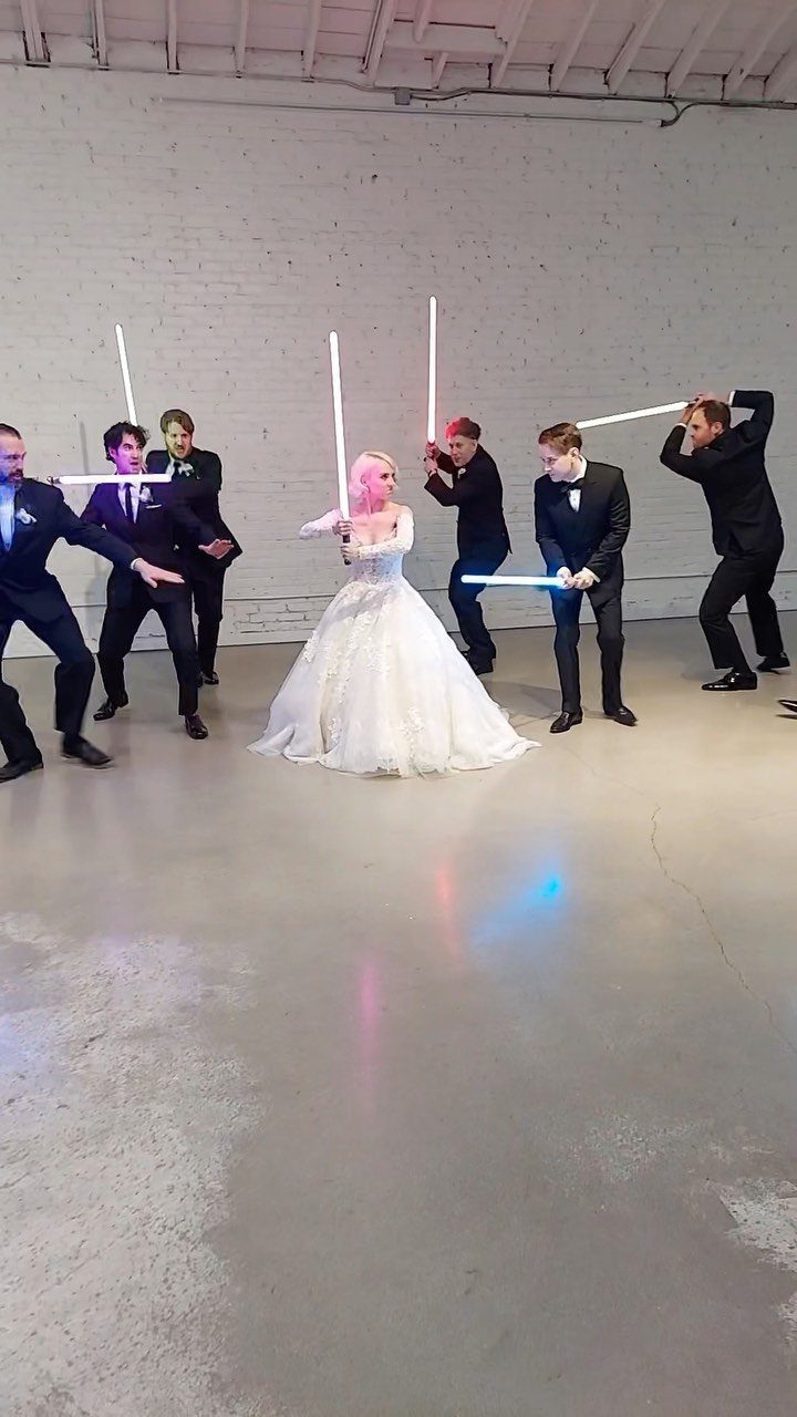 Bride and groomsmen posing with glowing white lightsabers in a white room.