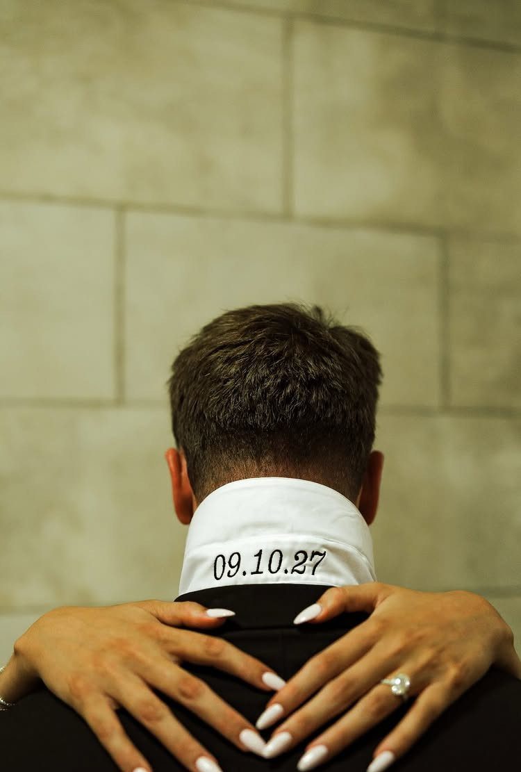 Man's collar with a date and woman's ringed hands on his shoulders.