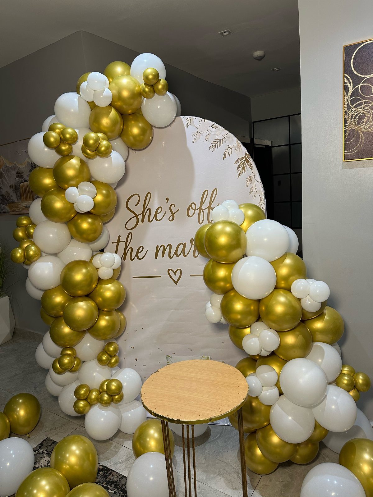 White circular backdrop with gold and white balloons and engagement announcement text.