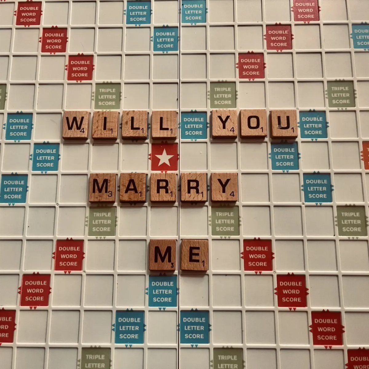 Wooden Scrabble tiles spelling Will You Marry Me on a game board