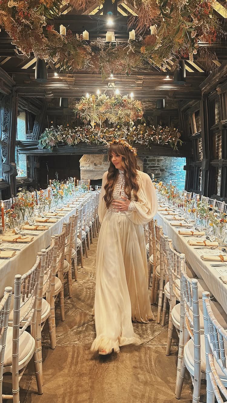 Woman in vintage bridal gown standing between long decorated tables in rustic room