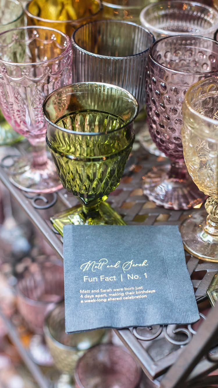 Colorful vintage pressed glass goblets and a gold-lettered napkin on a metal shelf