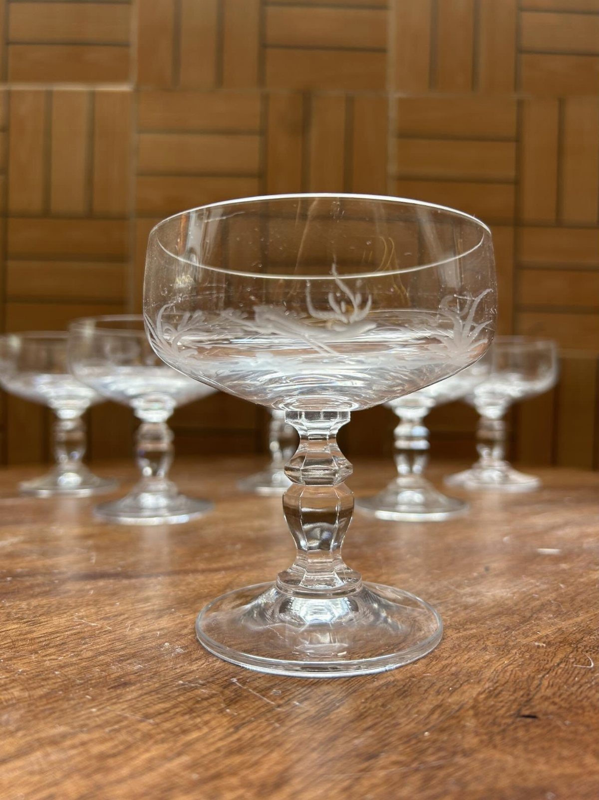 Etched glass coupe champagne glasses sitting on a rustic wooden table surface.