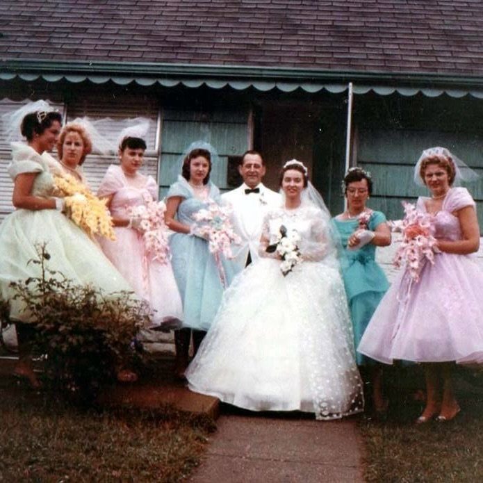 Wedding party in mid-century attire posing outdoors with a bride and groom.