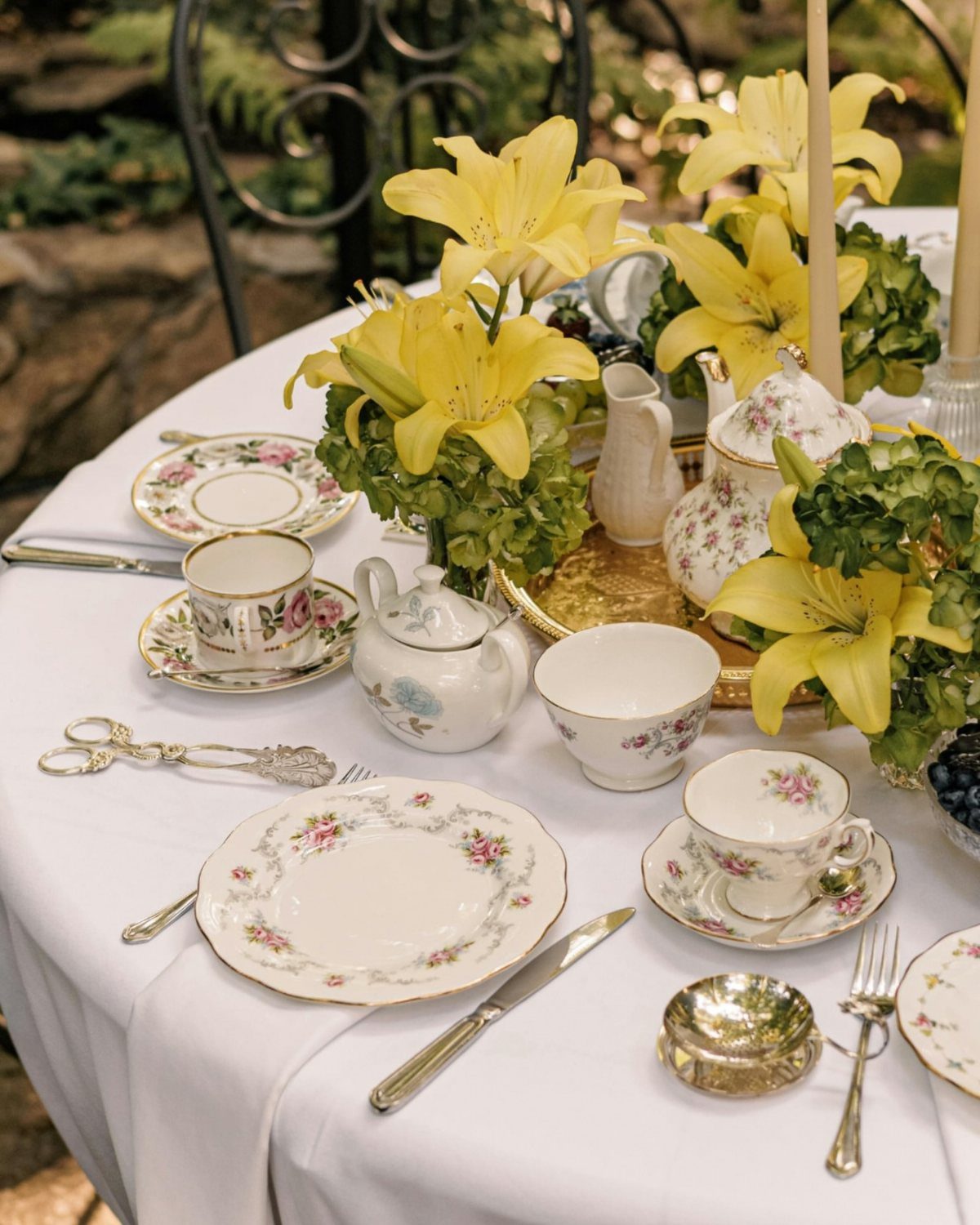 Floral china tableware and yellow lilies on a white wedding table setting.