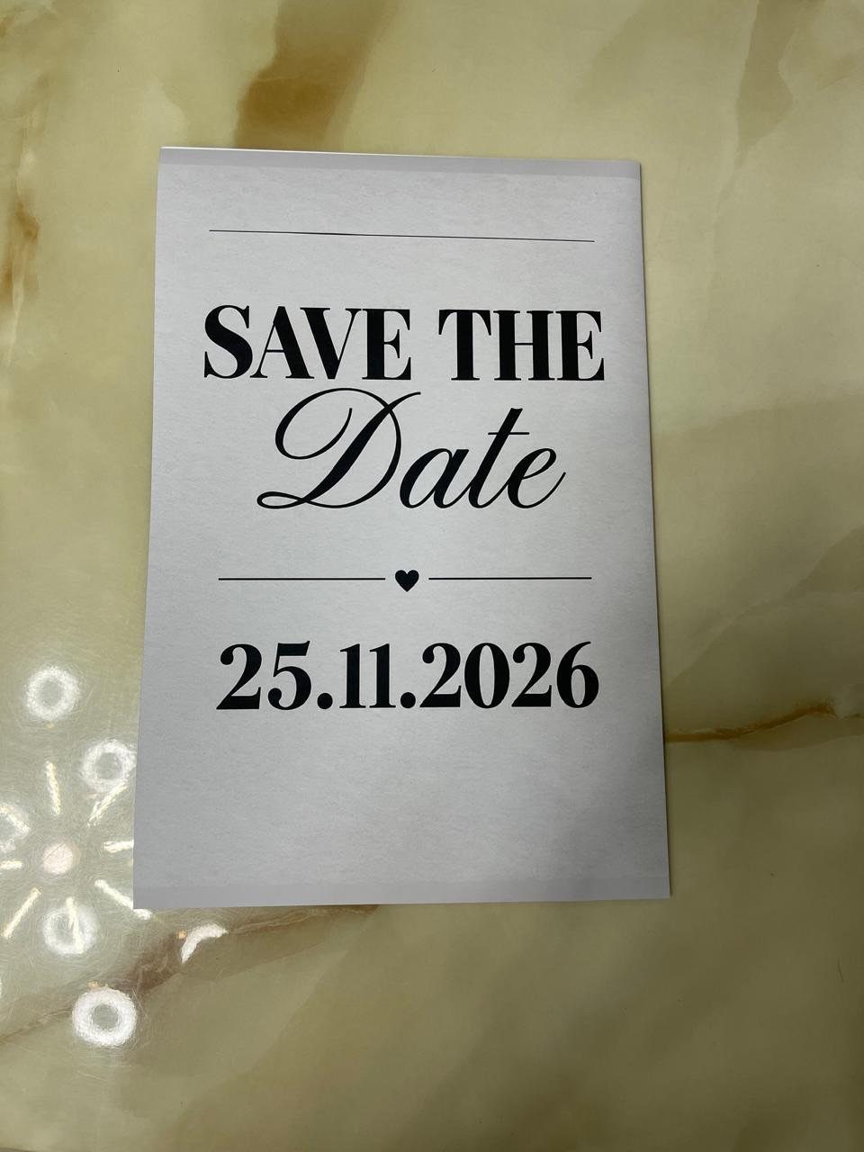 Save the date card with black text on a marbled beige surface