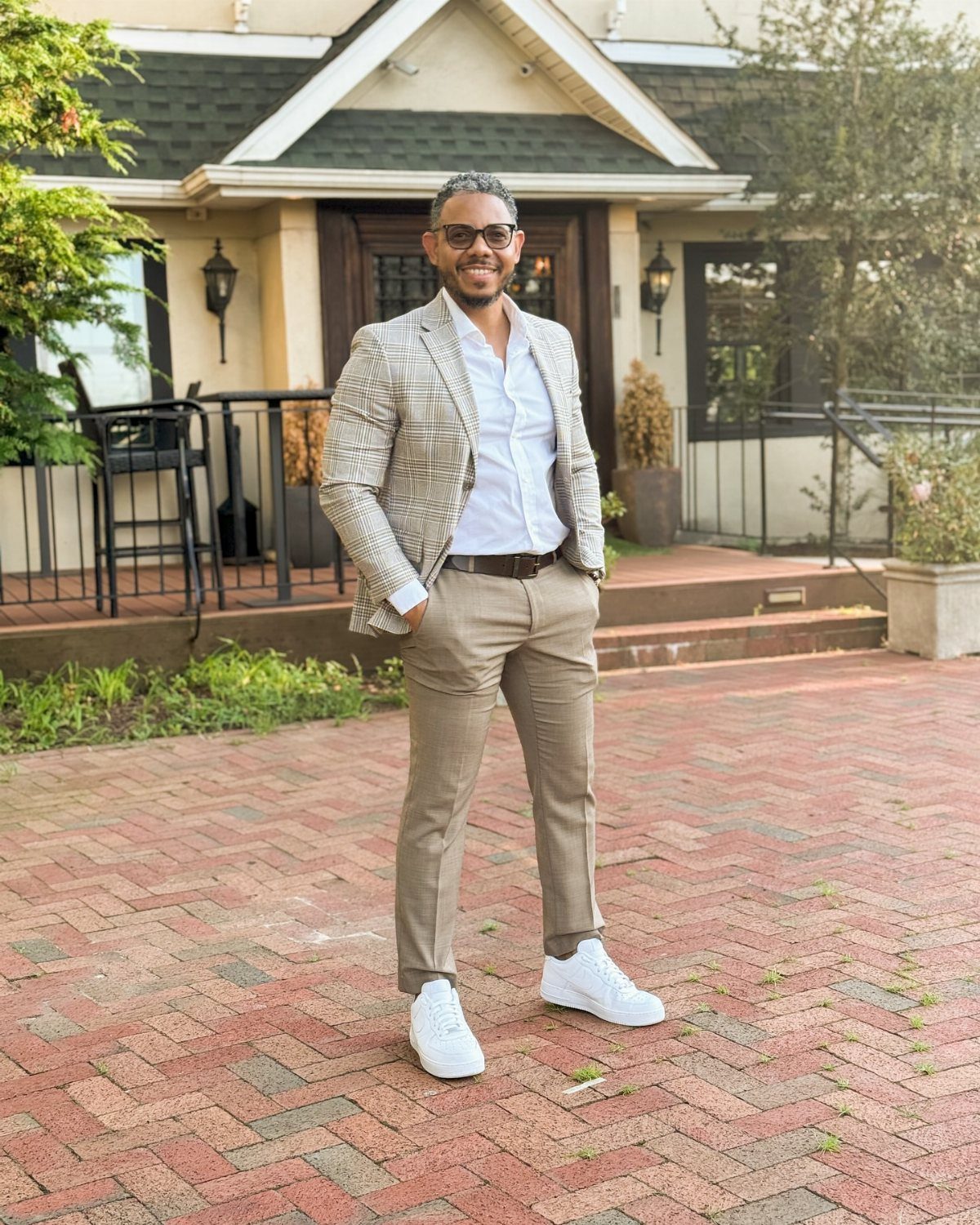 Man wearing a patterned blazer, khaki pants, and white sneakers on brick patio