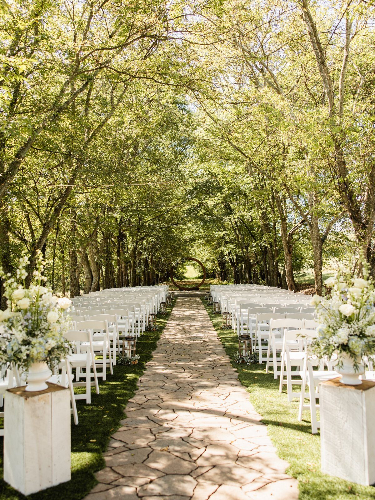 Outdoor wedding ceremony setup with white chairs and stone path in a wooded park