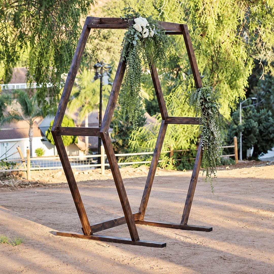 Wooden hexagonal wedding arbor decorated with white flowers and green foliage outdoors.