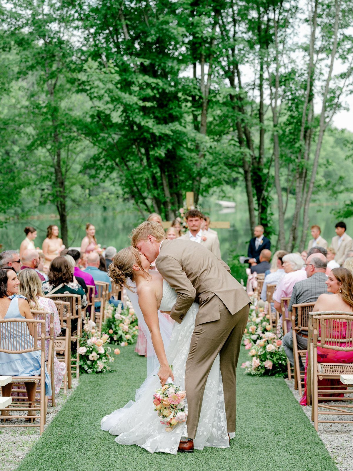 Bride and groom kissing at an outdoor wedding ceremony in a green park