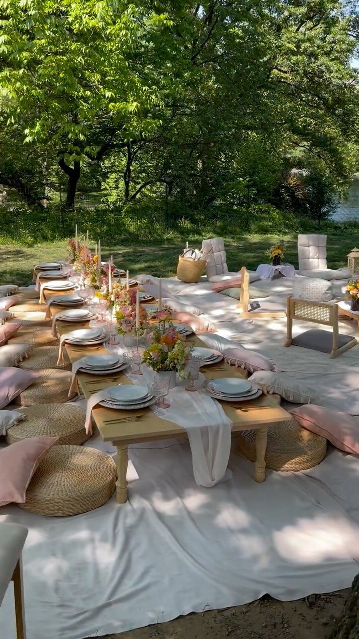 Low wooden dining table with floral centerpieces and floor cushions in a park
