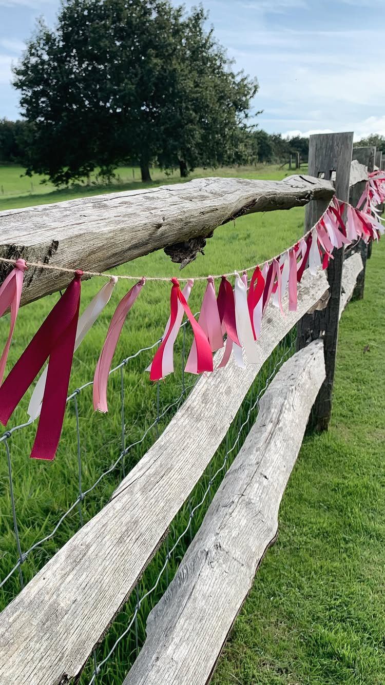 Pink and white ribbon garland draped across a rustic wooden fence in a field