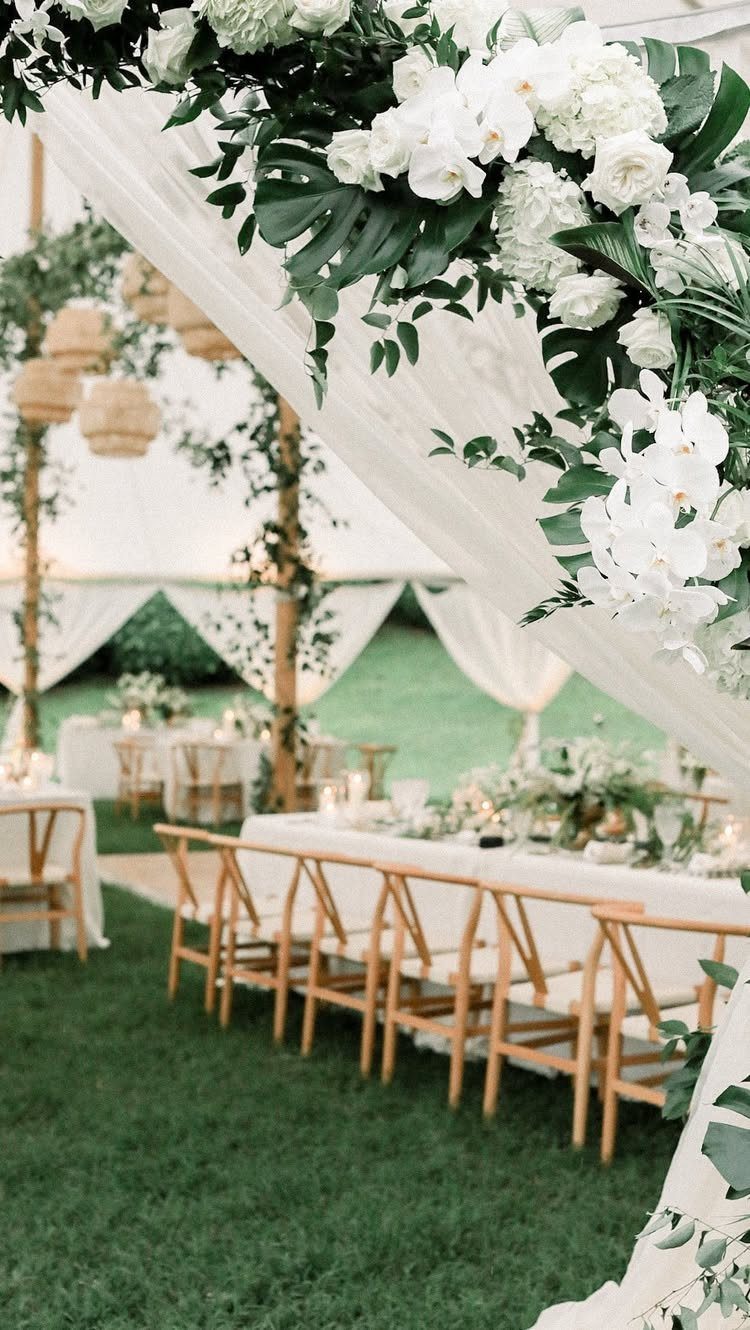 White wedding tent with floral draping and wooden chairs on a green lawn