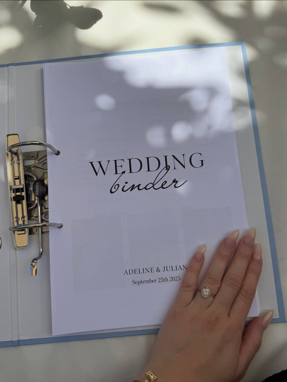 Wedding binder title page with names and date, held by a woman's hand.