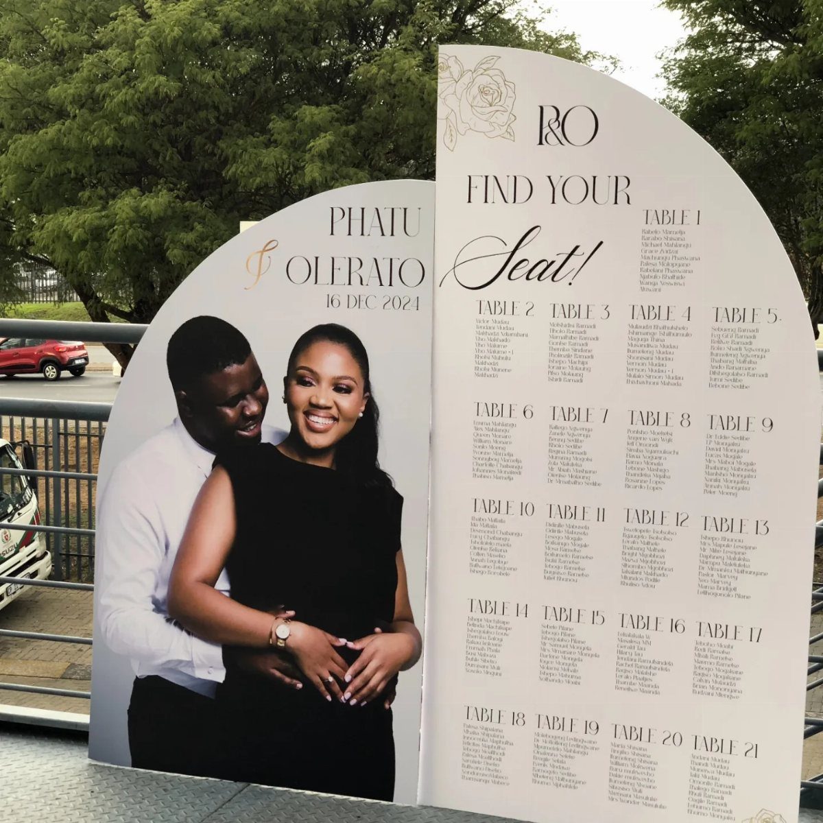 Wedding seating chart sign with a couple's photo and guest table assignments.