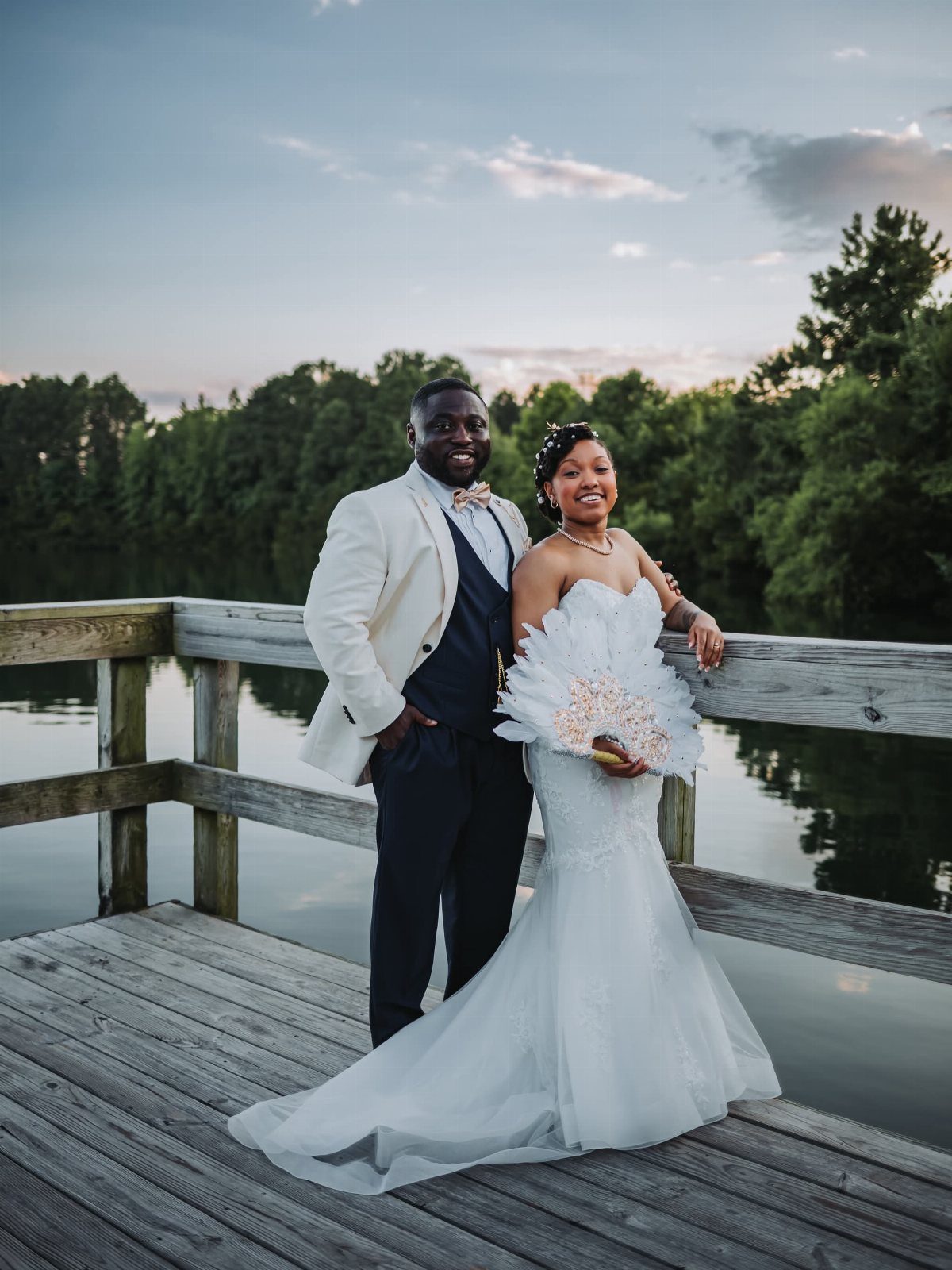 Bride and groom posing on a wooden pier by a calm lake.