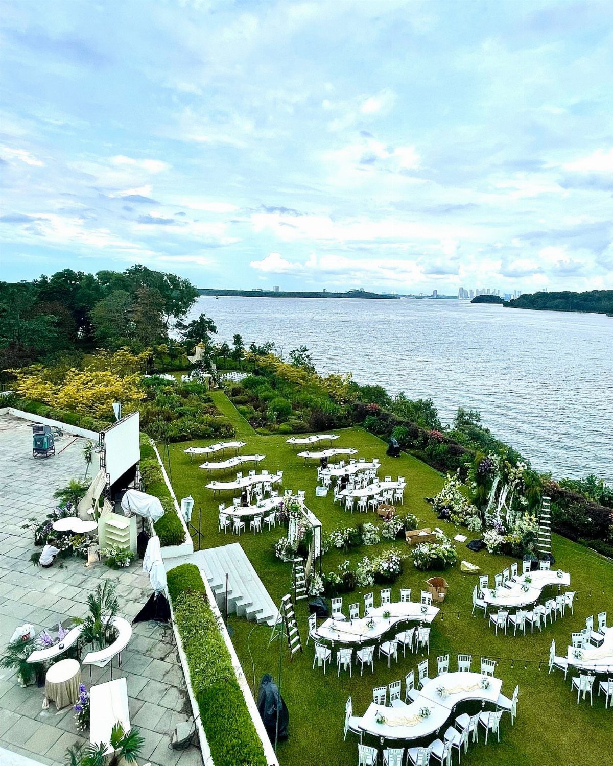 Outdoor wedding reception setup with white tables and chairs on a riverside lawn.