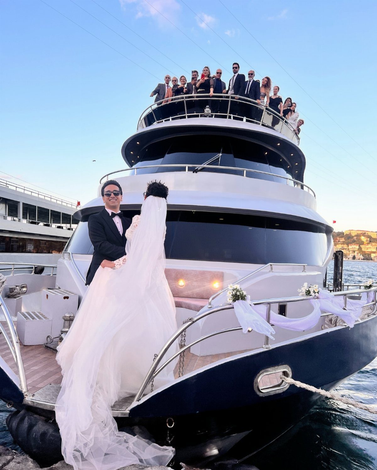 Bride and groom posing on the deck of a luxury yacht with guests.