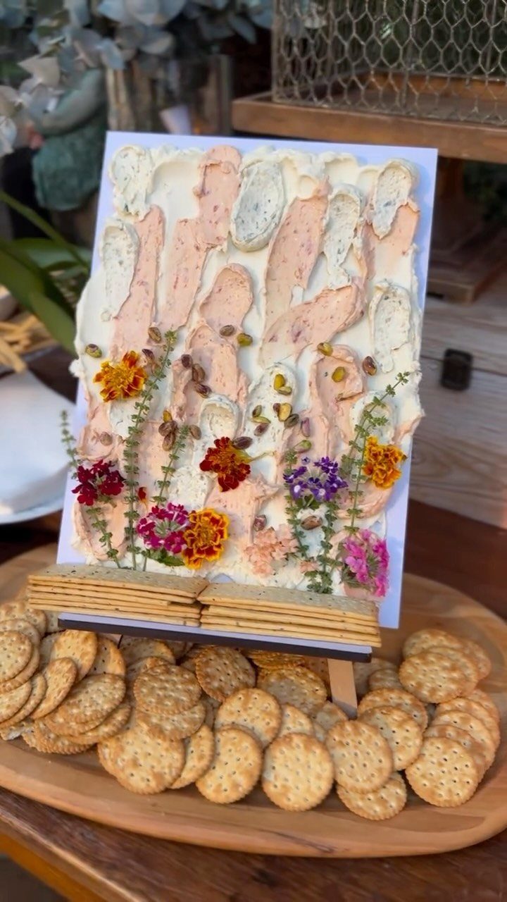 Artistic cream cheese dip board with edible flowers and crackers on wooden platter