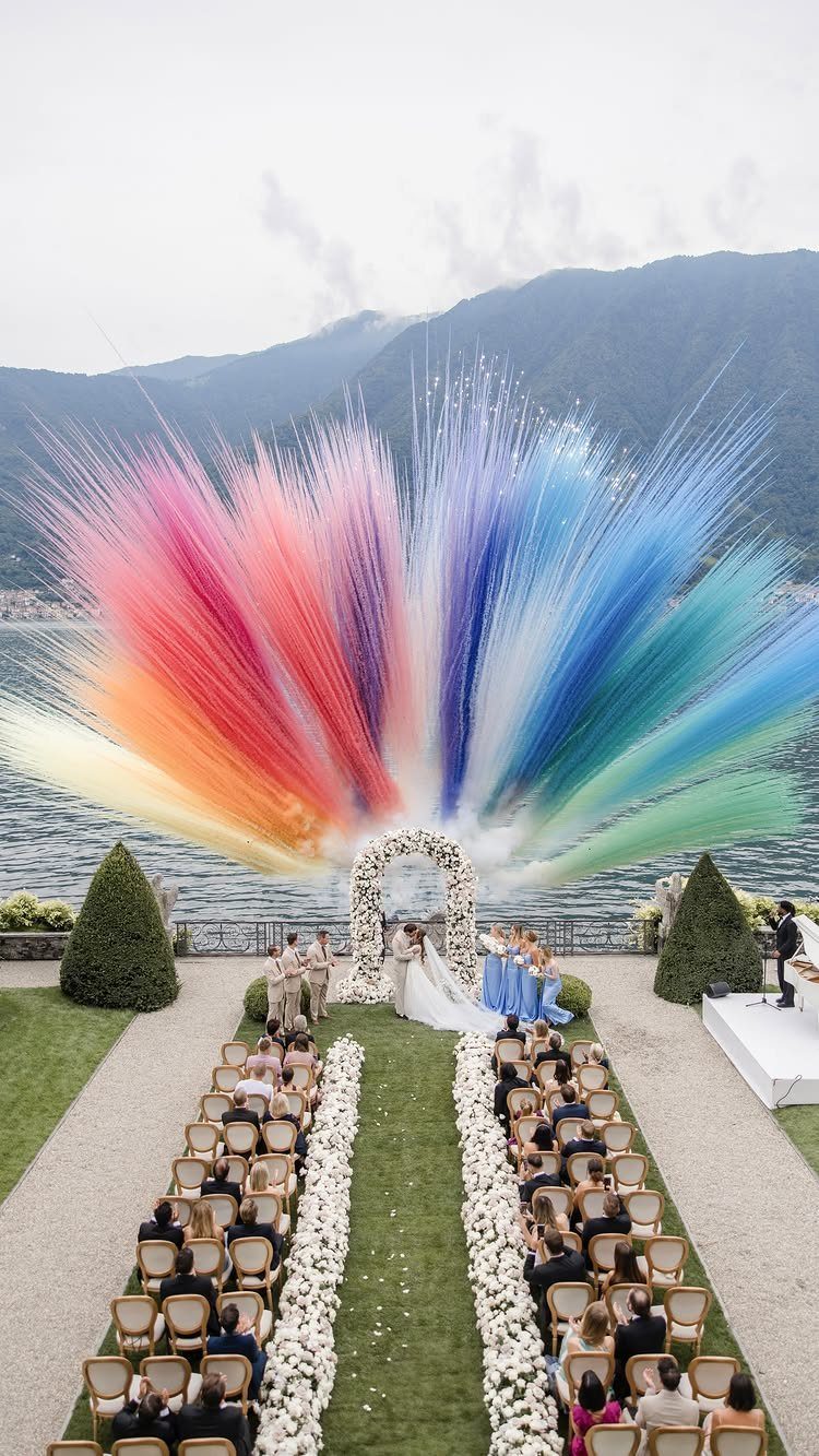 Wedding couple under floral arch with a giant rainbow powder explosion overhead.