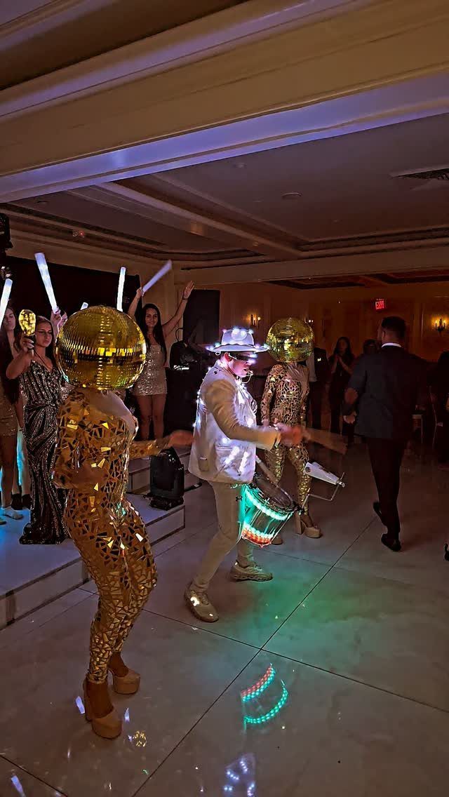 Performers in gold sequined outfits and spherical headpieces dancing at a wedding celebration.