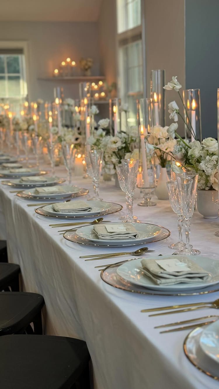 Long dining table set with white linens, grey plates, gold cutlery, and candles.