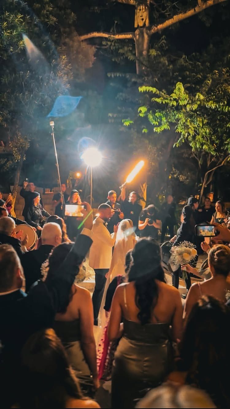 Wedding couple standing outdoors at night with a fire performer holding a torch.
