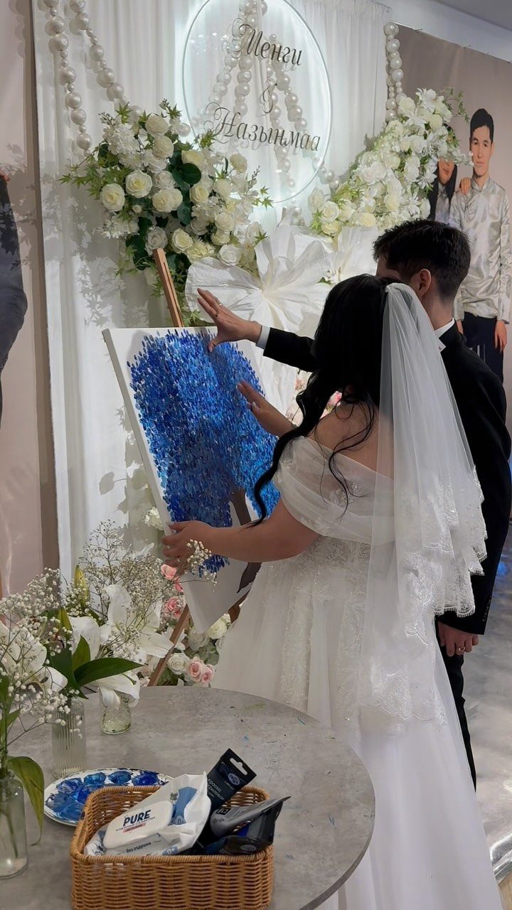 Bride and groom painting a blue textured canvas at their wedding celebration.